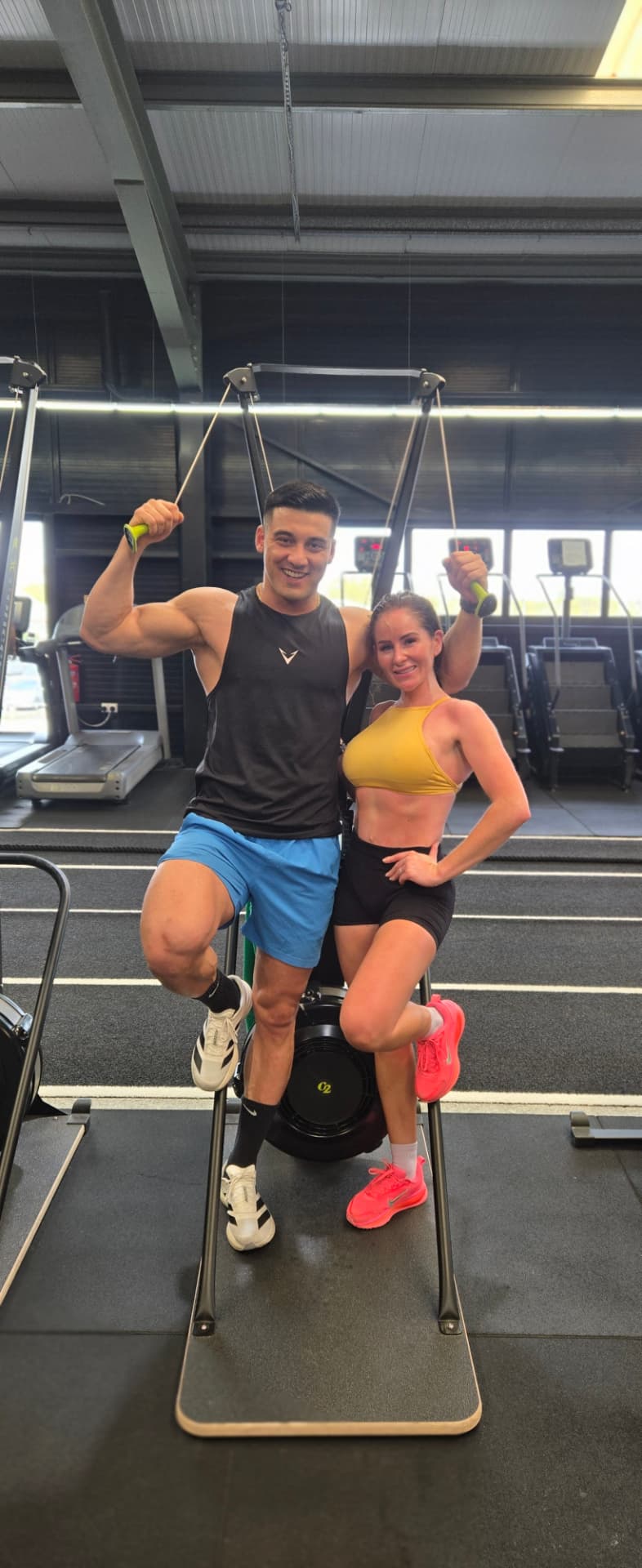 Coach M.M.X and a client flexing on gym equipment