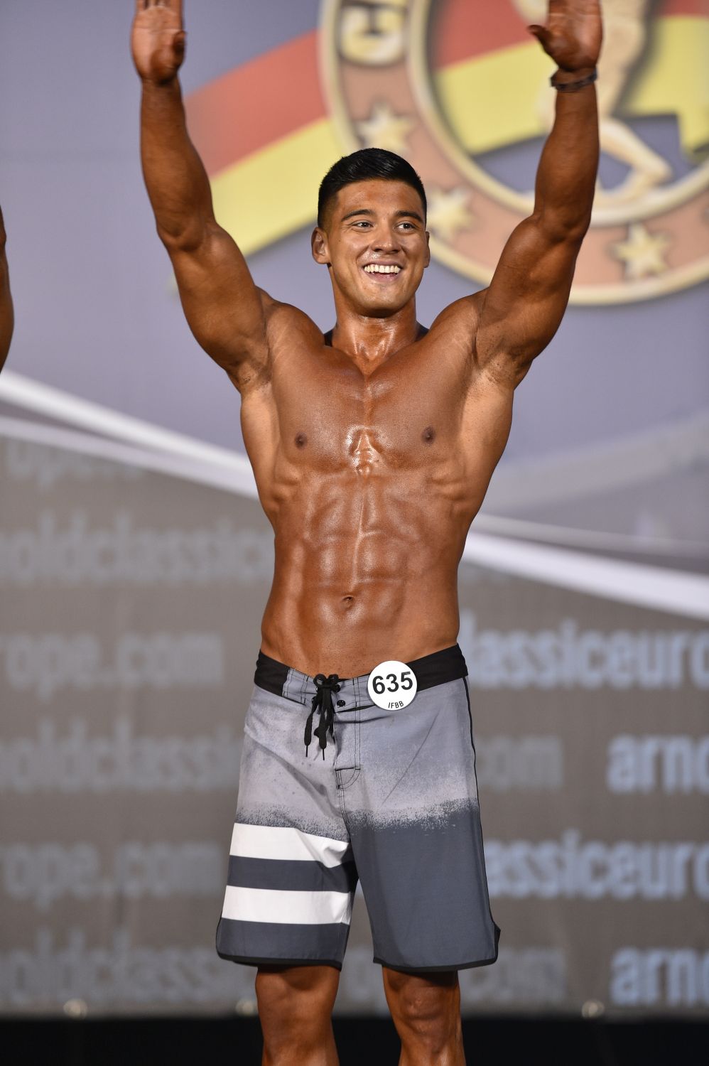 Coach M.M.X celebrating with arms raised on stage at Arnold Classic Europe