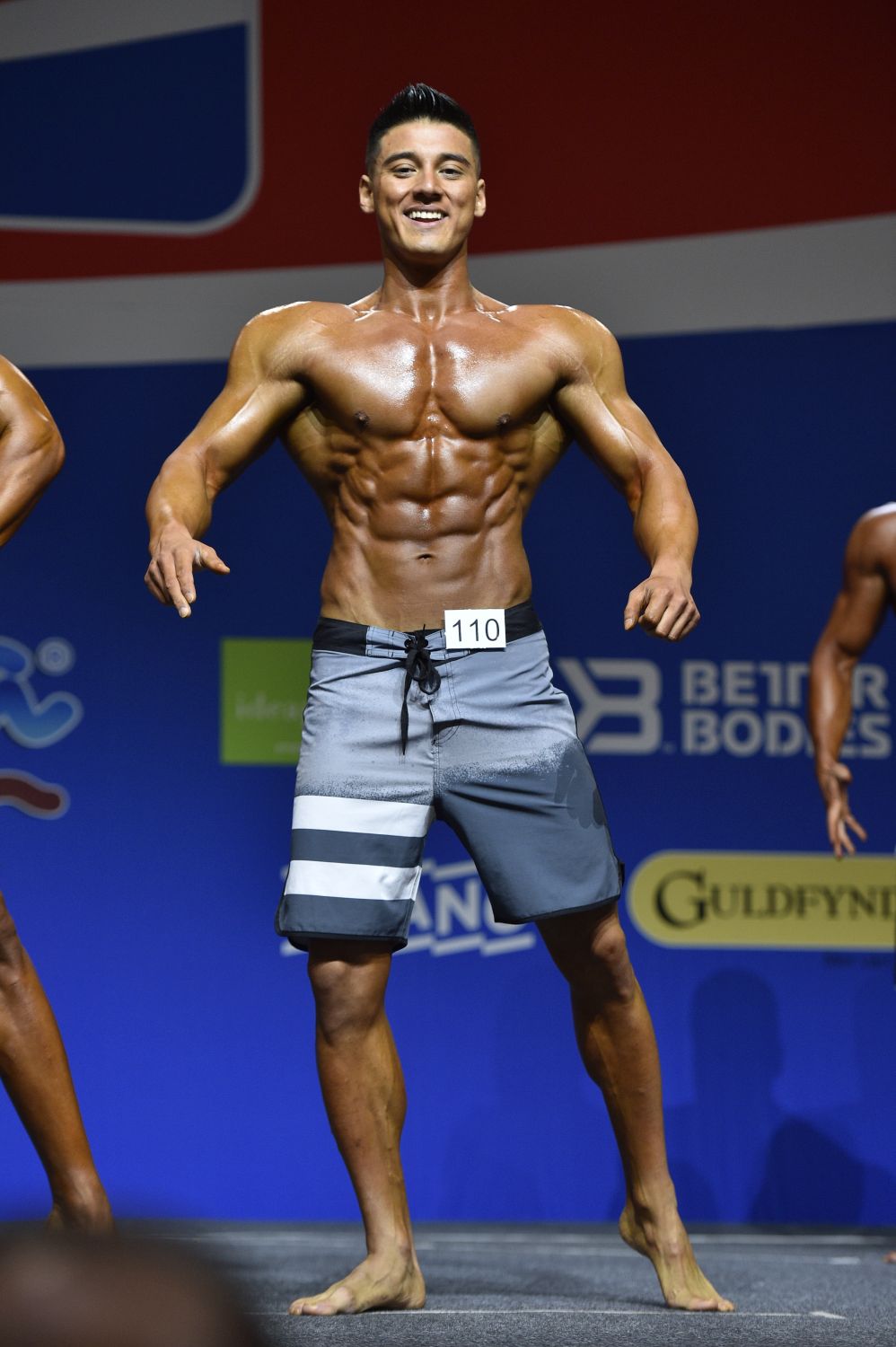Coach M.M.X in men's physique posing on stage at an international competition